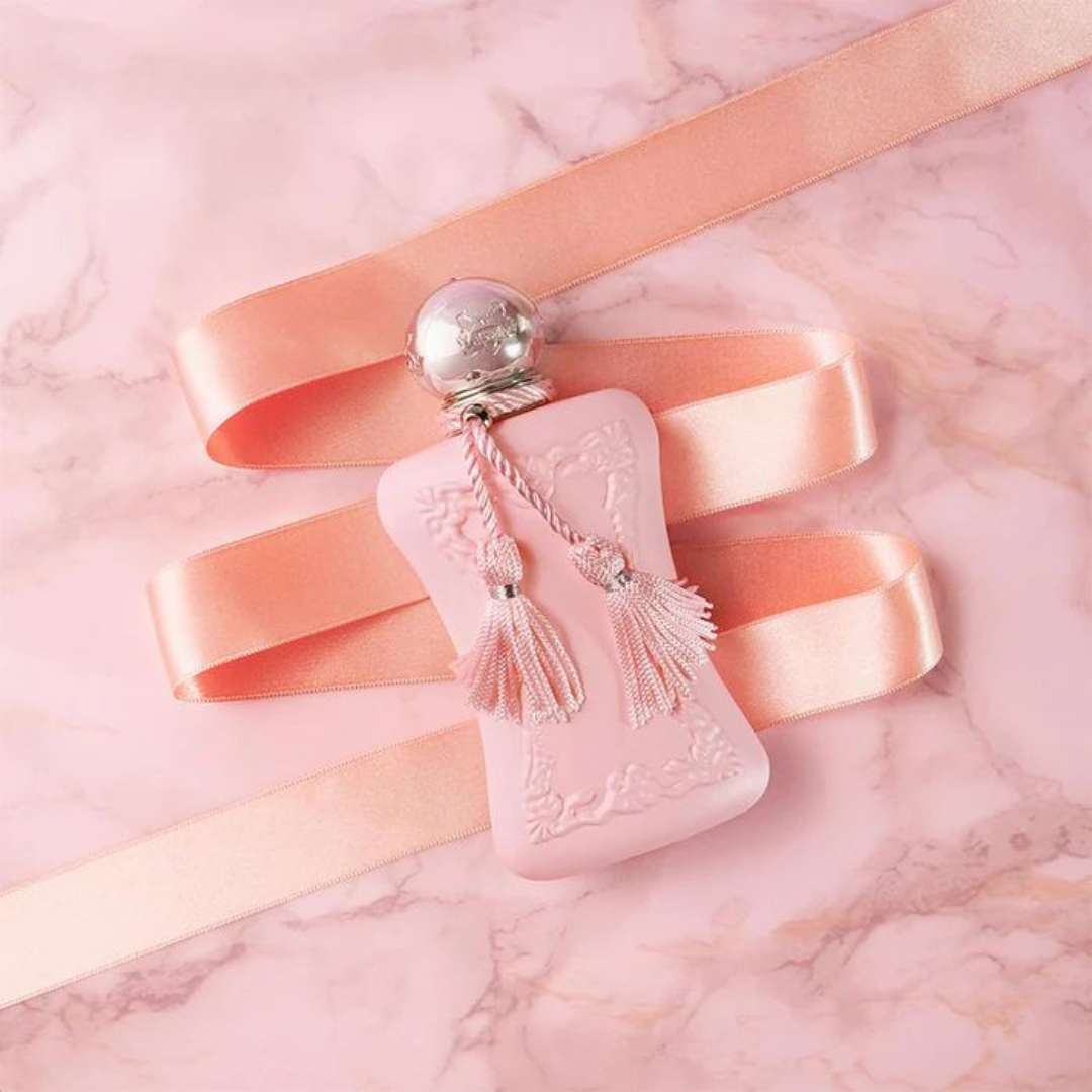 Pink perfume bottle with tassels and a silver cap on a pink satin ribbon against a pink marble background.