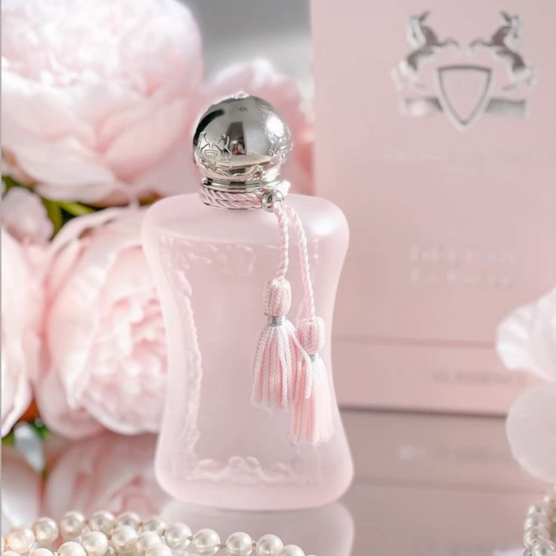 Pink perfume bottle with silver cap and tassel, surrounded by pink flowers and pearls.