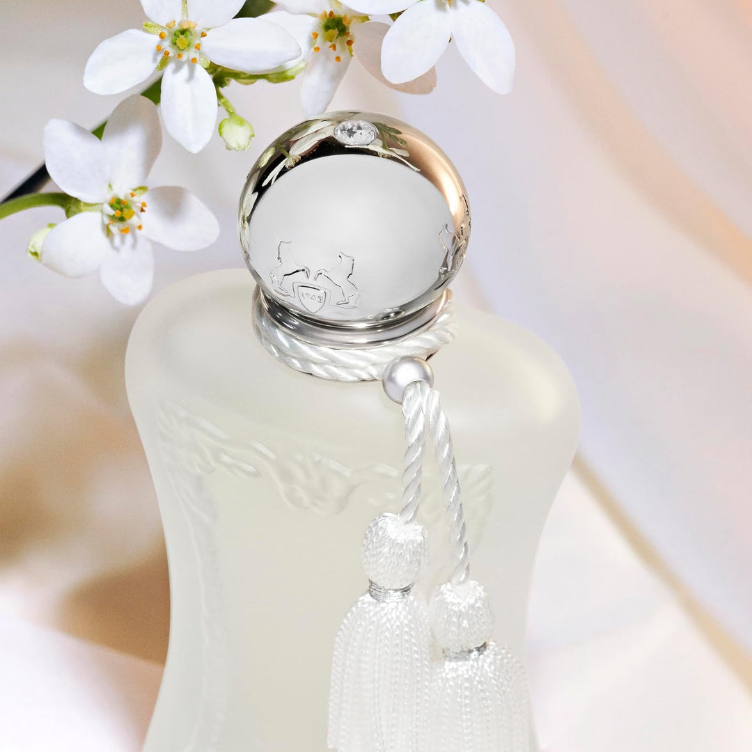 White perfume bottle with silver cap and tassel, surrounded by white flowers.