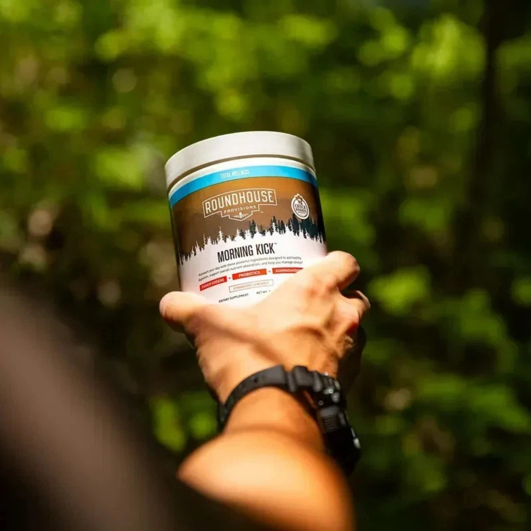 Hand holding a 'Roundhouse' product container with a blurred green background