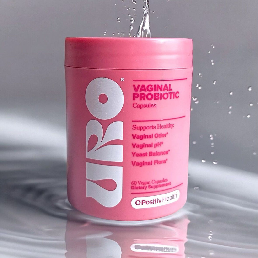 Pink container of vaginal probiotic capsules with water droplets on a gray background